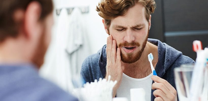 man with tooth pain while brushing his teeth