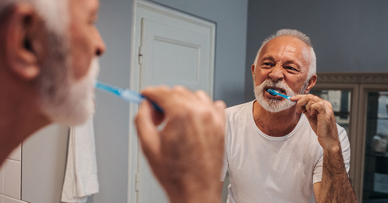 man practicing good oral hygiene at home by brushing his teeth in the mirror
