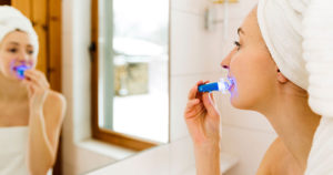 woman look at bathroom mirror while using a home teeth whitening kit, a popular but questionable home remedy for teeth