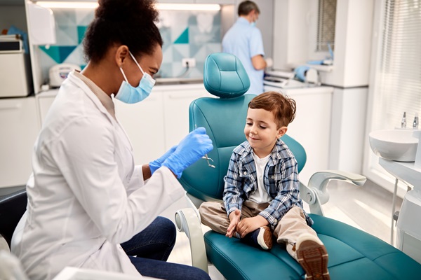 Little boy talking to African American female dentist during appointment at dental clinic.