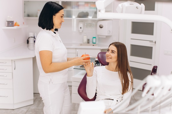 Female dentist smiles and gives an apple to a girl patient in de