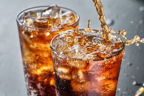 two cups of cola soft drink being poured into glass