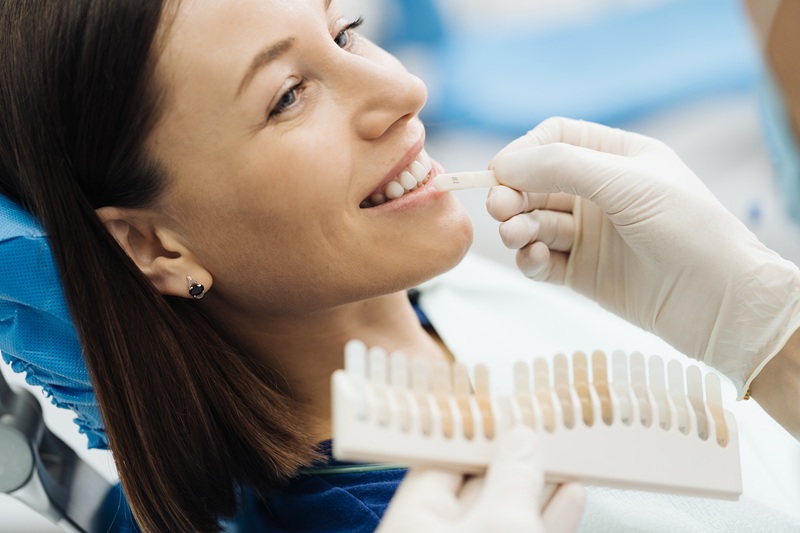 Dentist checking and selecting color of young woman's teeth