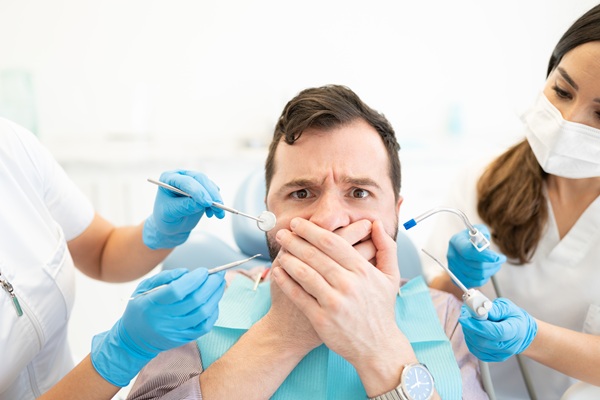 Frightened mid adult man covering mouth while dentist holding tools during treatment
