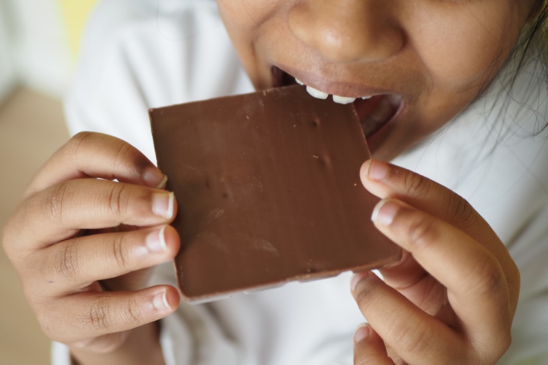 A girl is about to eat a piece of chocolate while relaxed at home.