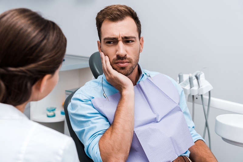 selective focus of upset patient touching face while having toothache near dentist