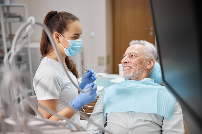 Senior citizen smiling while sitting in a dental chair and looking at his young dental specialist